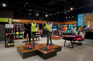 Manichini in pose dinamiche su pedane rialzate illuminate con abbigliamento running fluo giallo e rosa