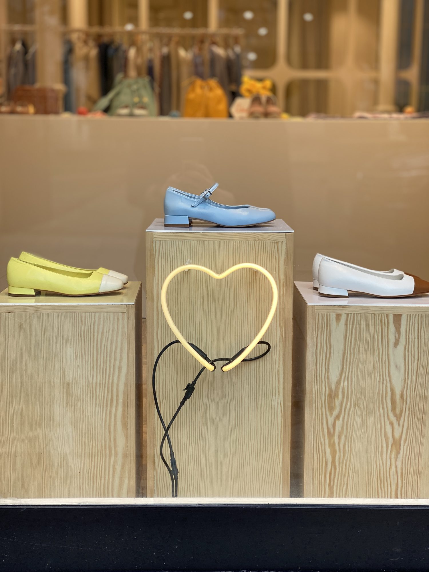 Sky blue Pocca Mary Janes on a pine plinth with a neon heart in the window