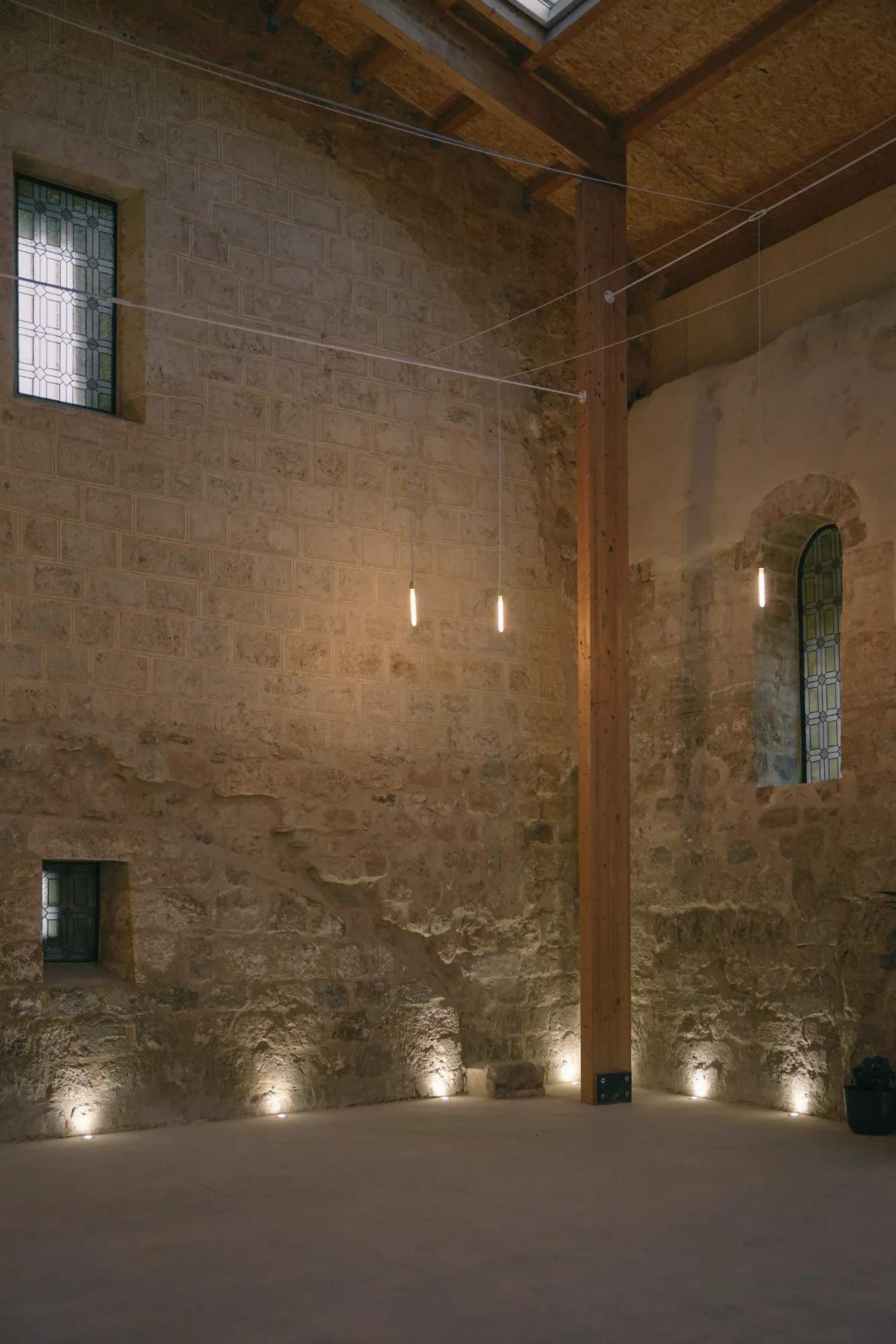 Stone walls lit from below by floor spotlights and linear pendants